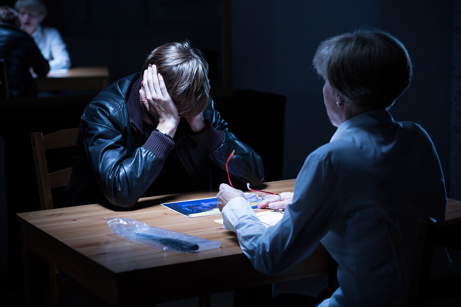 Woman discussing juvenile crimes with a young man in a black leather jacket in a dark police interrogation room.