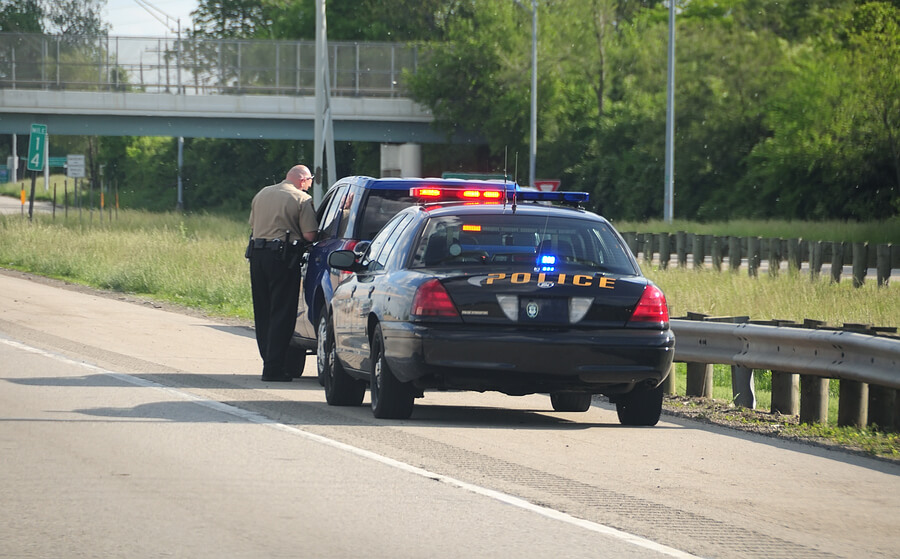 Police officer pulling a blue car over on the side of the road to give them Raleigh, NC traffic tickets.